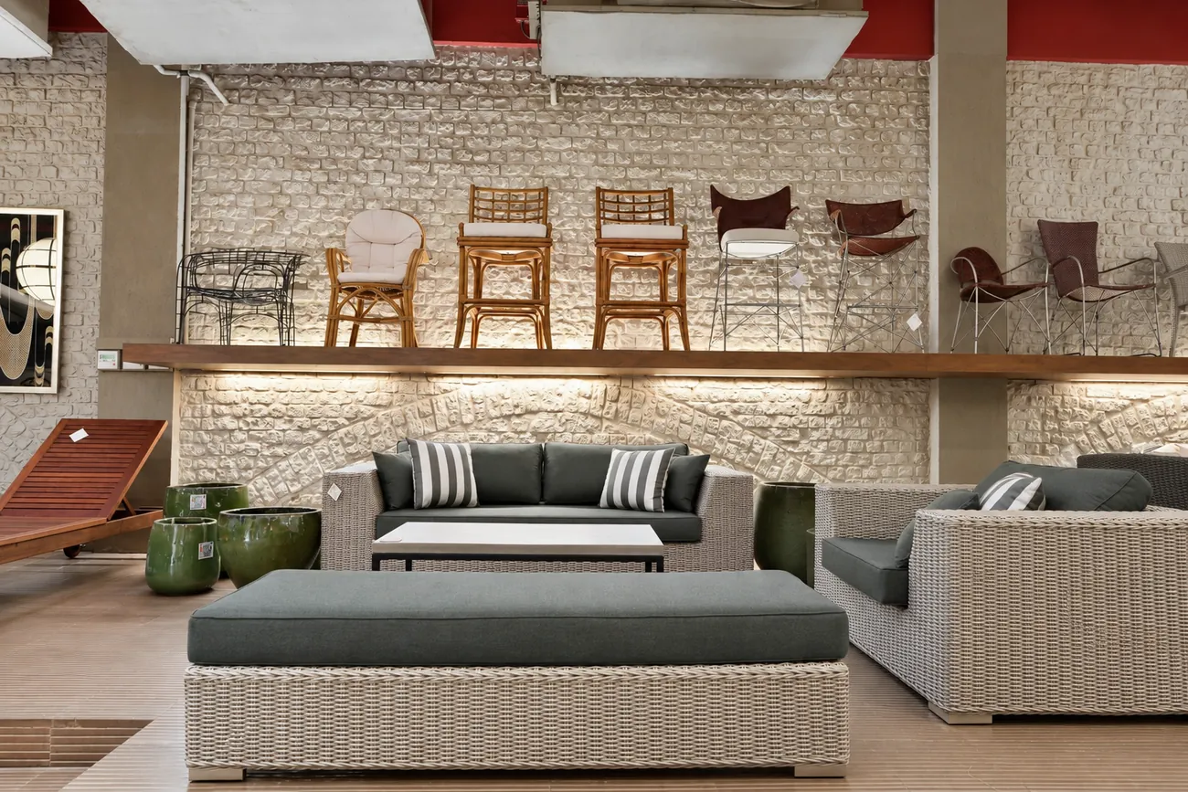 Textured stone wall at Abaca lined with a shelf of outdoor chairs above a grey wicker sofa and green ceramic planters.