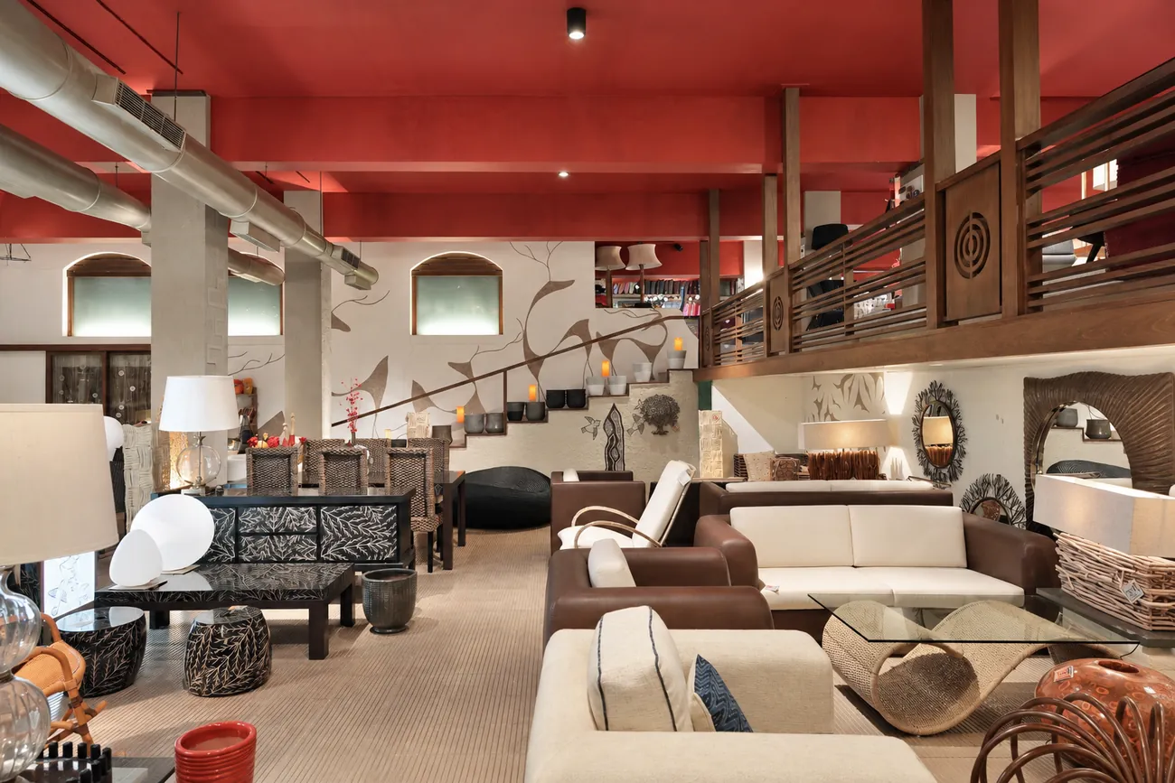 Wide view of the Abaca showroom with a bold red ceiling over the industrial mill volume, furniture arranged across the open floor.