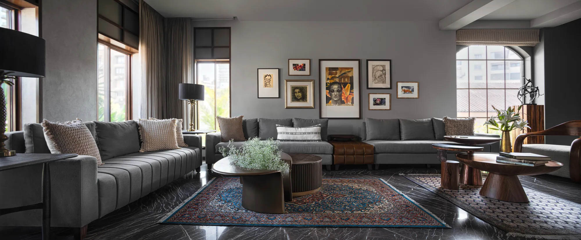 Panoramic view of the living room at Cambridge Court: grey sofas around sculpted coffee tables, a gallery wall of framed works, and an arched window with a bronze sculpture on a timber plinth.