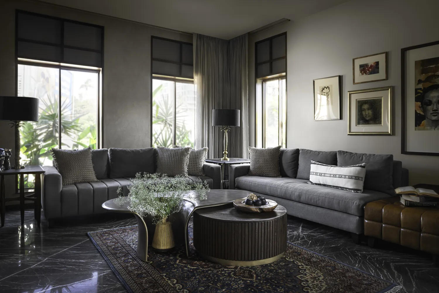 Living room at Cambridge Court with grey sofas, black lamps on brass palm stands, a fluted timber drum table and a Persian rug on dark marble.