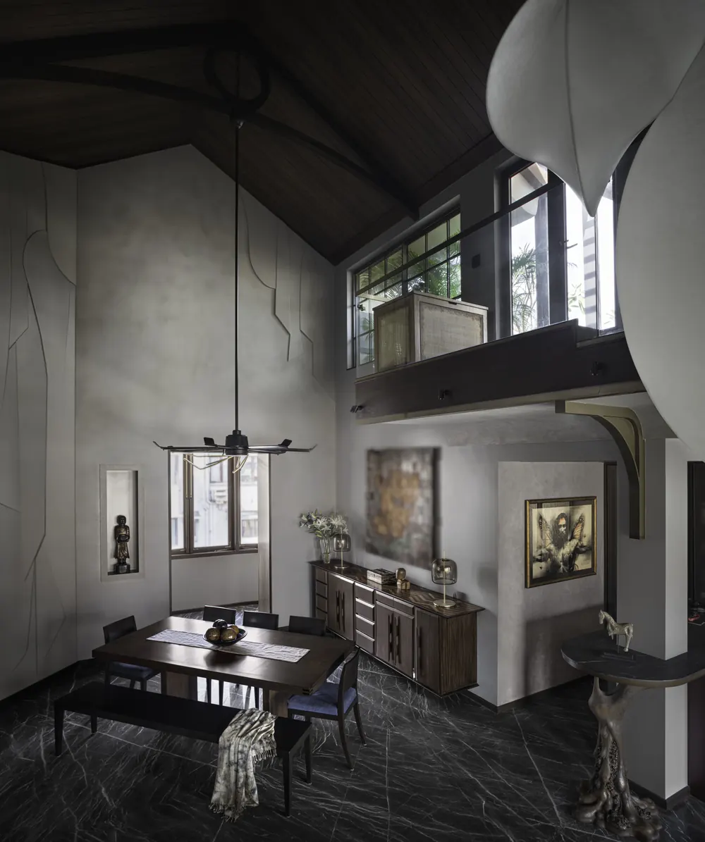 Dining area at Cambridge Court under a restored timber pitched roof, with a sculpted grey plaster wall and a mezzanine window above.