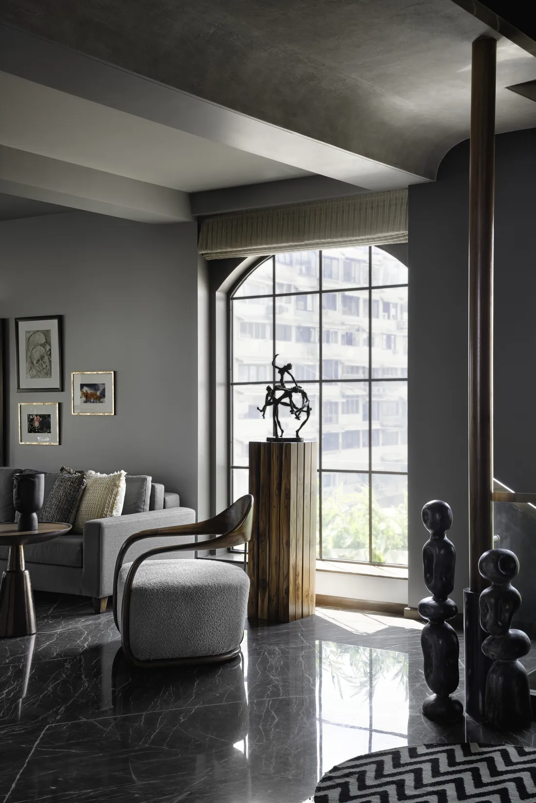 Corner of the living room at Cambridge Court: a bronze figure sculpture on a timber plinth before an arched steel window, a curved timber armchair and dark carved totems beside the stair.