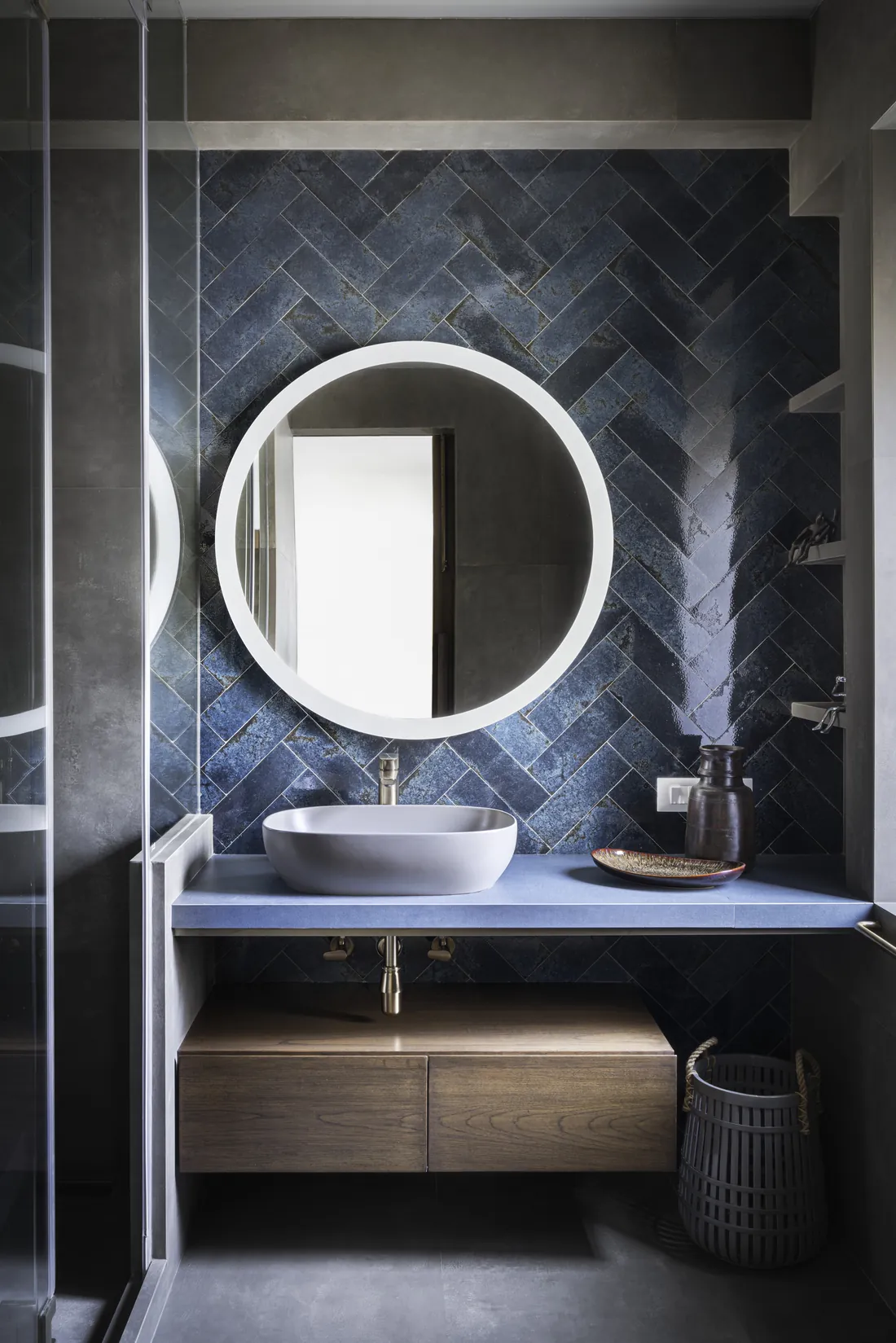 A second bathroom at Cambridge Court, with a round backlit mirror set against a deep blue herringbone-tiled wall.