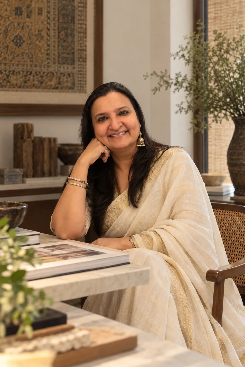 Roopali Mashruwala smiling, seated at a stone-topped table in a designed interior.