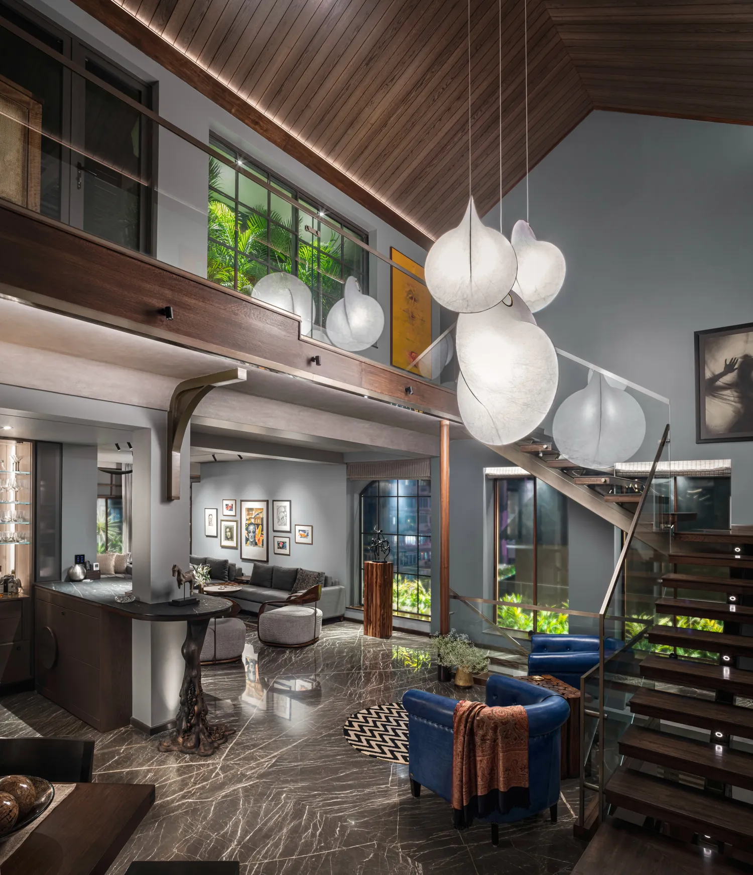 Double-height living space at Cambridge Court beneath the restored timber roof, with cocoon-shaped paper pendant lights, a steel and timber stair, an art wall and blue leather armchairs.