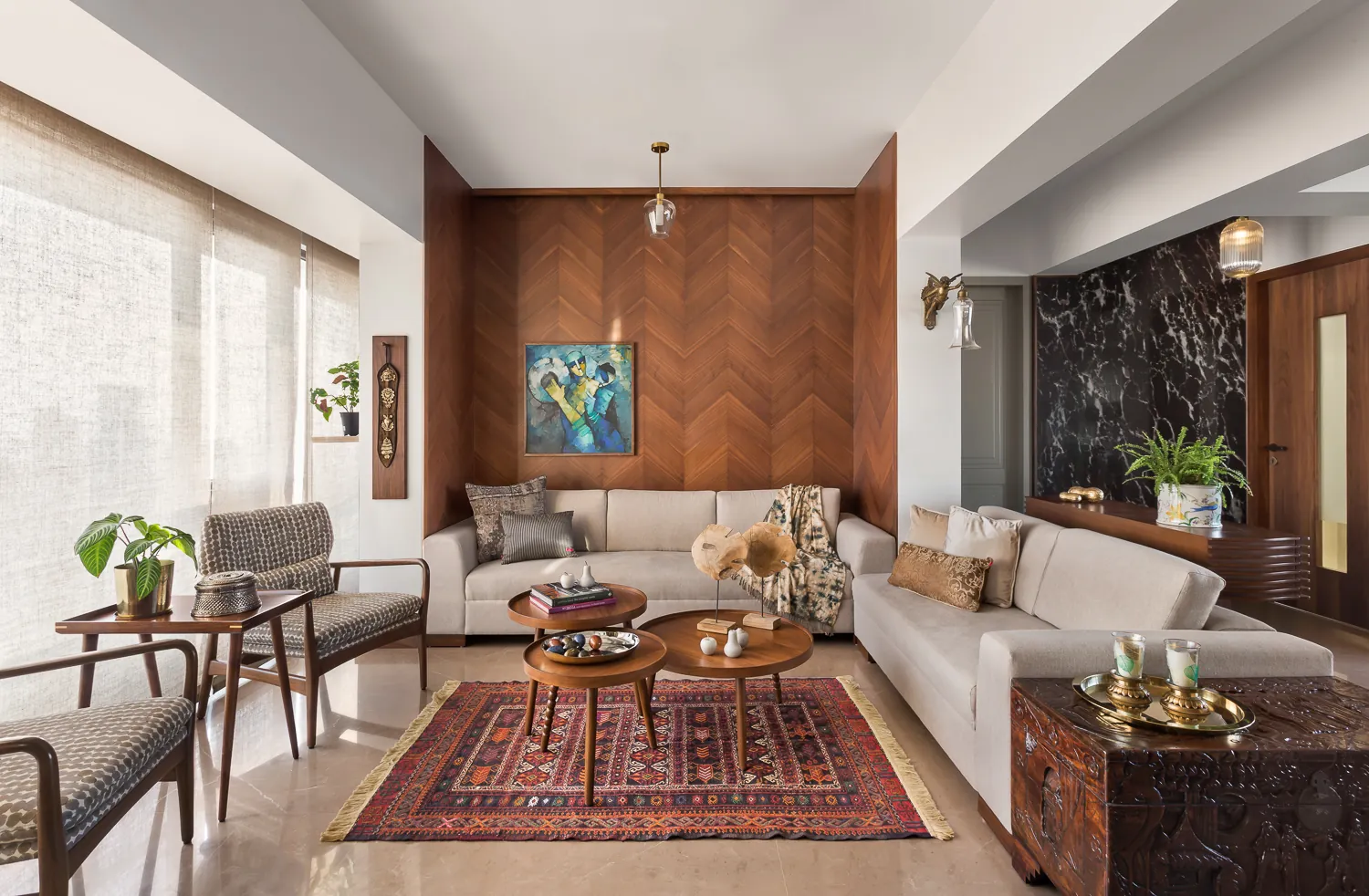 Living room at Zara with a walnut chevron-panelled feature wall, a framed figurative painting, beige sofas and a patterned Kilim rug.