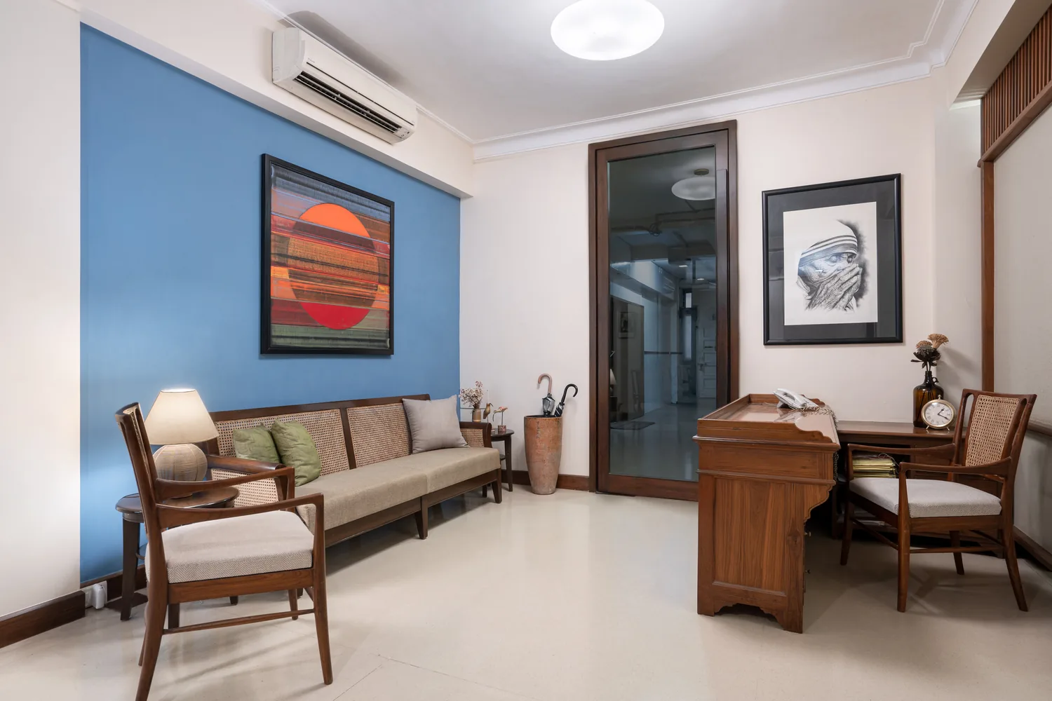 Reception and seating area at Lawyers Chambers with a blue accent wall, a framed abstract painting, cane-backed chairs and a writing desk.