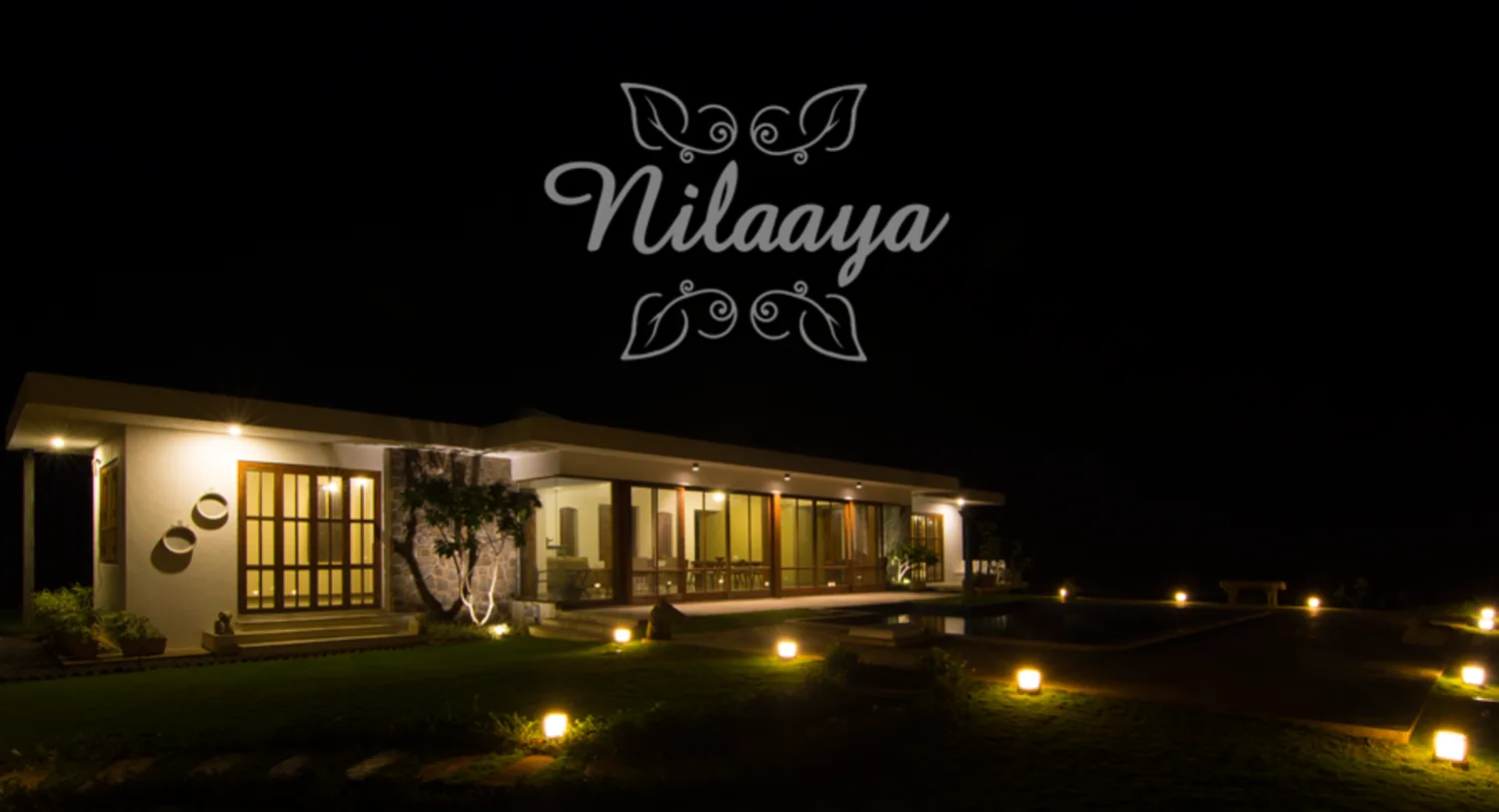 Nilaaya at night, its glazed living spaces lit from within, with the pool and garden lanterns in the foreground.