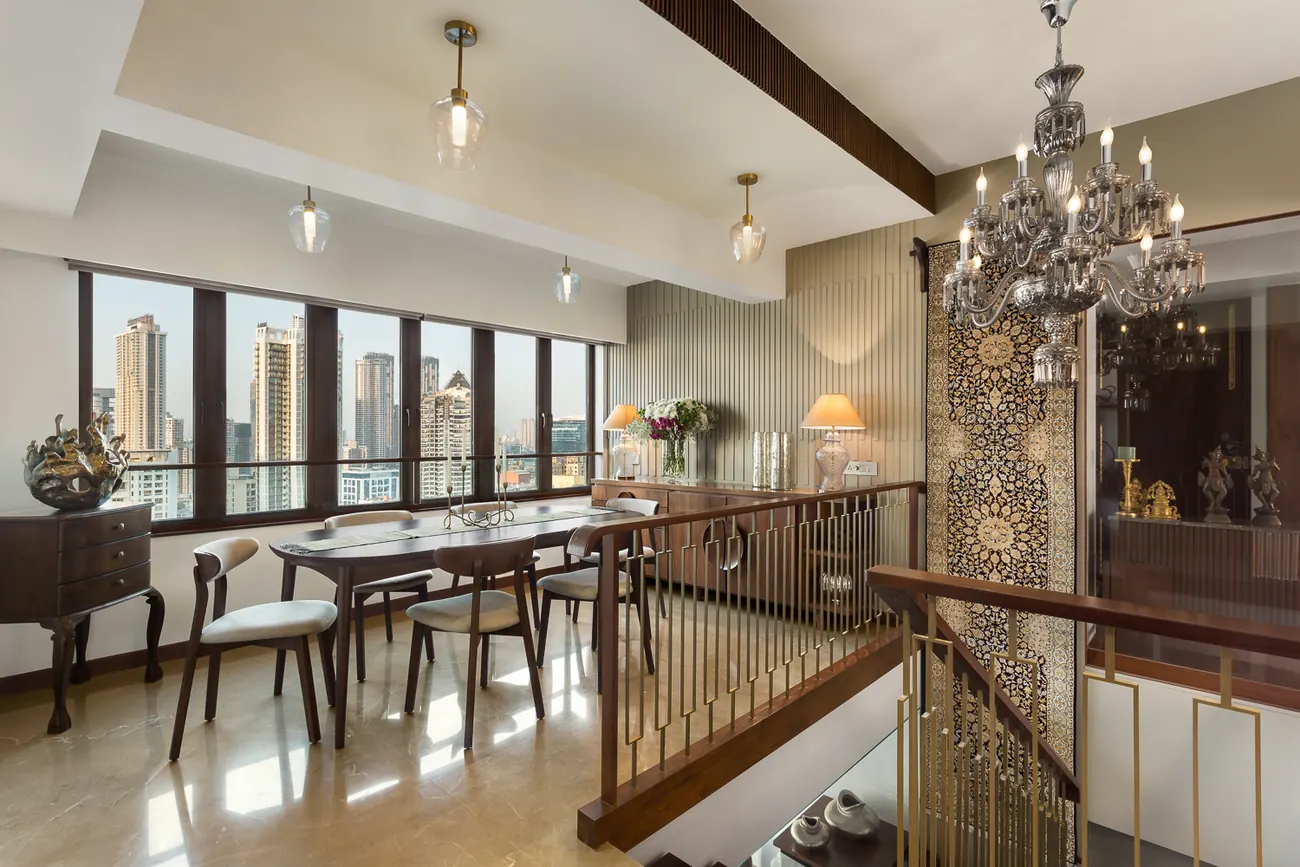 Dining area at Zara with an oval table, a crystal chandelier, a brass and timber stair railing and a hanging textile.