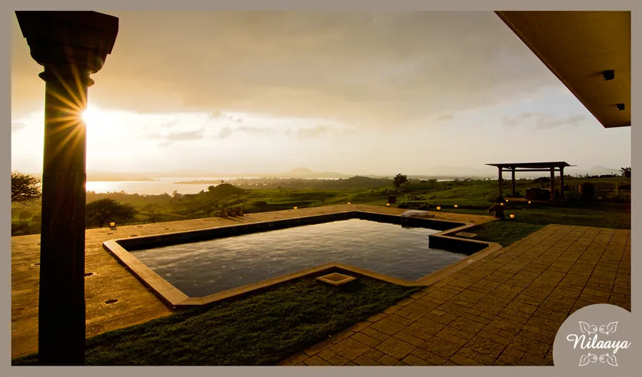 Swimming pool at Nilaaya at sunset, seen past a stone column, with hills in the distance.