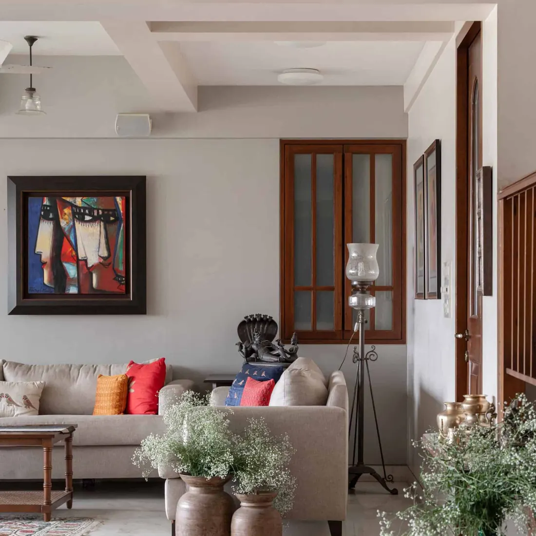 Living room at Lloyds Gardens with a linen sofa, a framed contemporary painting, a teak-framed internal window and a standing glass lamp.