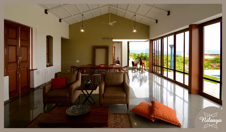 Entrance hall at Nilaaya with a glazed stone floor, dining table, horse sculptures and full-height glass doors opening to the garden and pool.