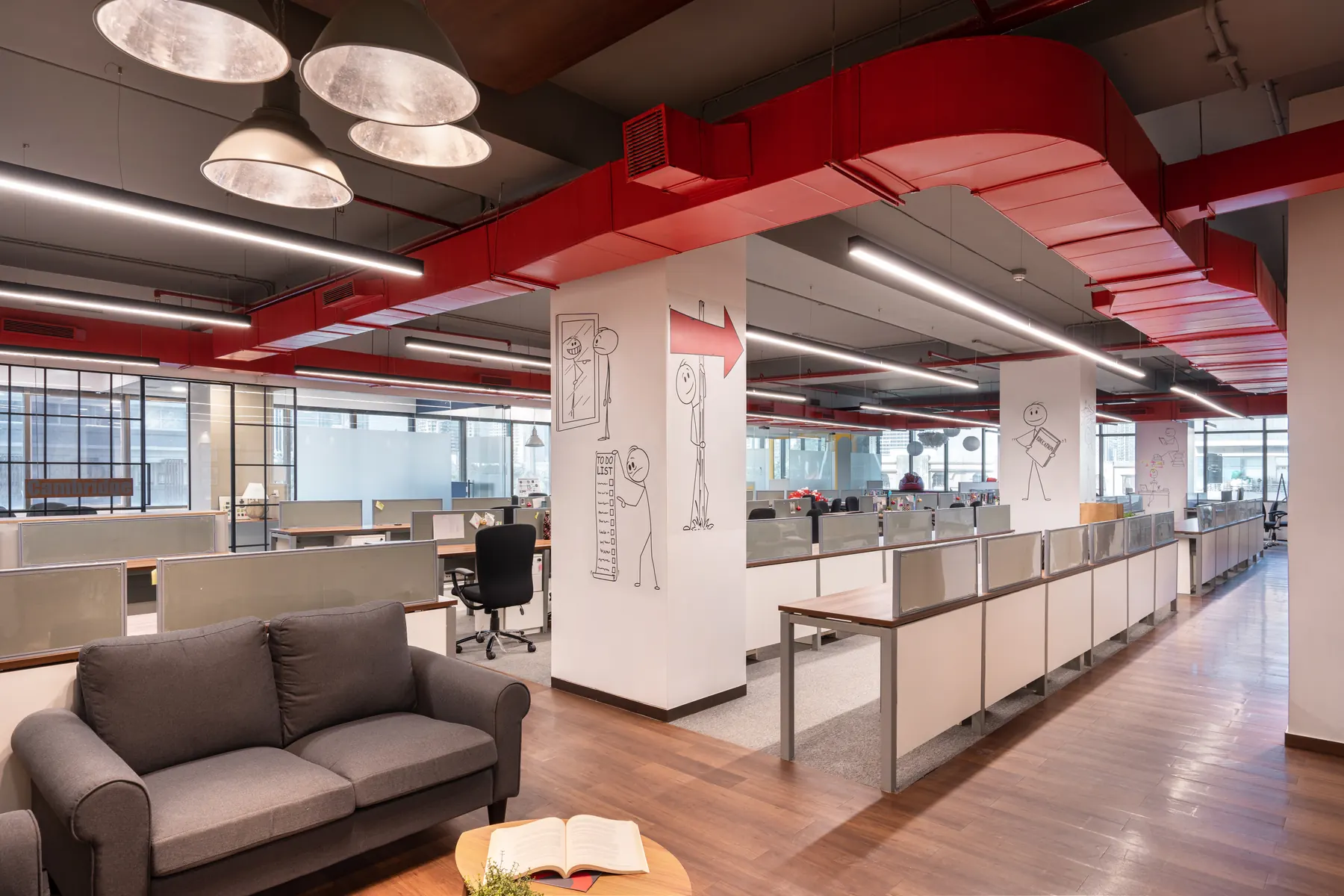 Open-plan OnCourse office in Worli: red ducts arch over white columns drawn with line figures, with pendant lamps and a grey sofa in the foreground.