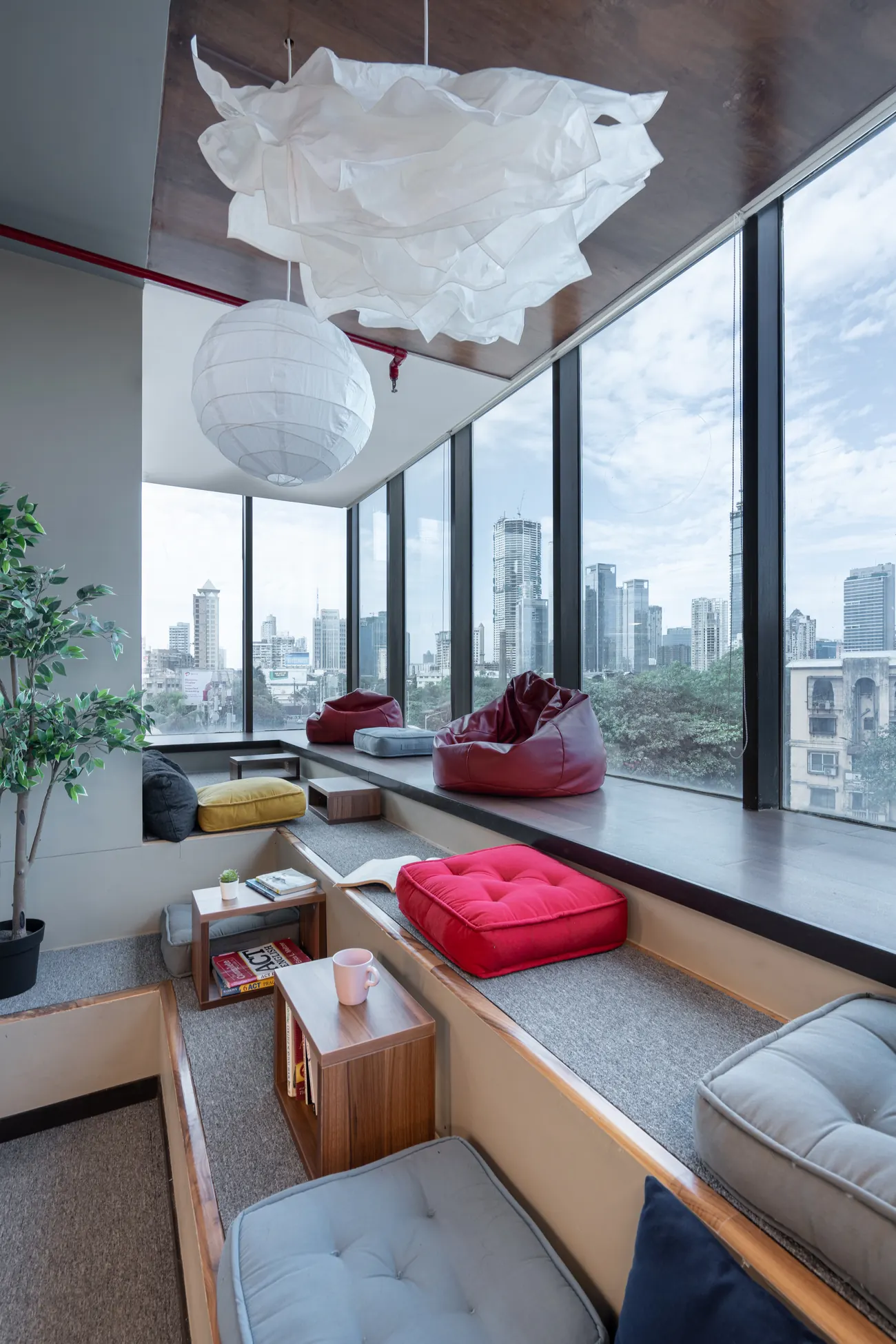 Informal seating nook at OnCourse with leather bean bags and floor cushions by a floor-to-ceiling window overlooking Mumbai.