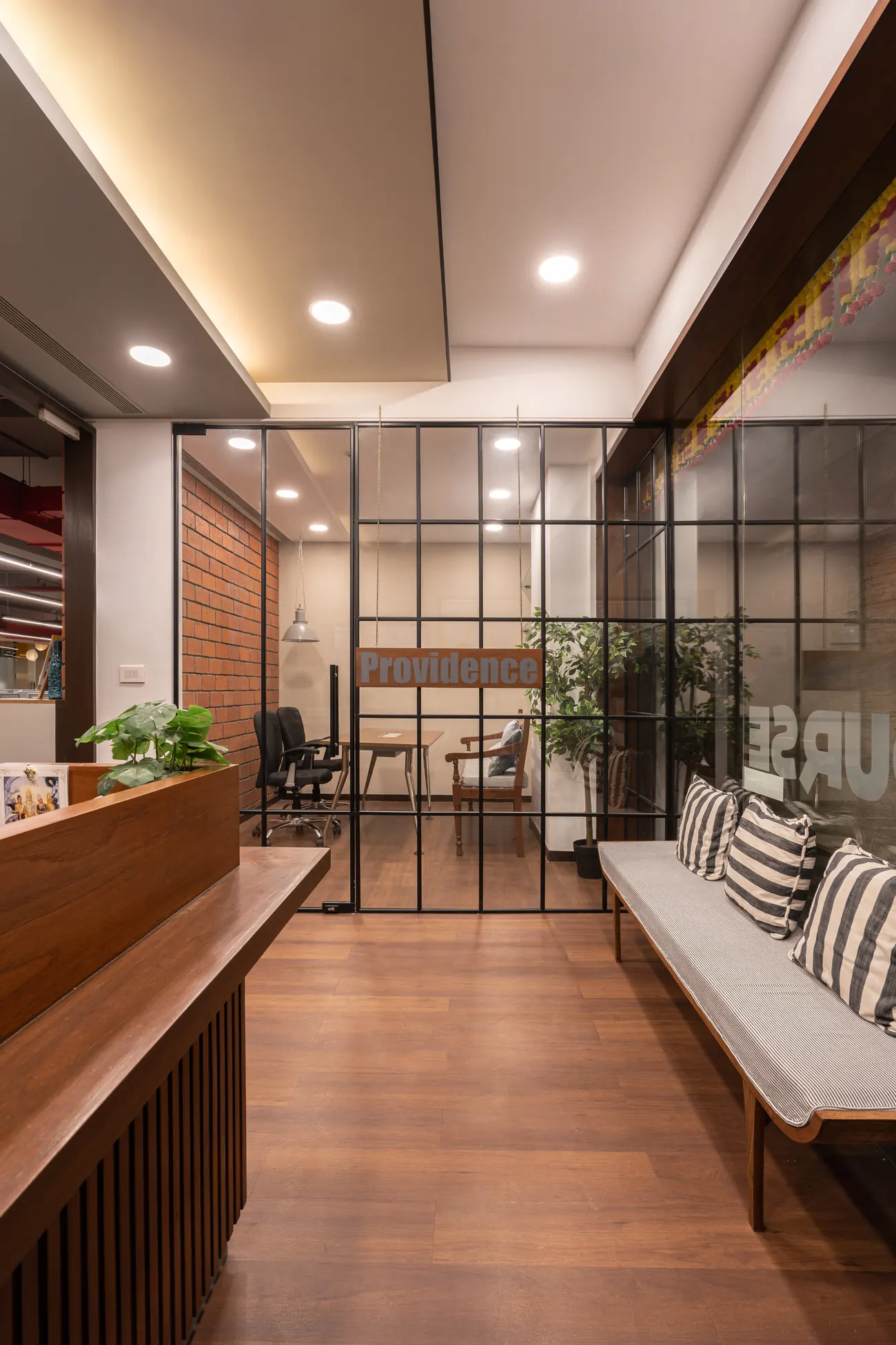 Corridor at OnCourse with a glazed meeting room, hanging Claremont sign and open-plan desks beyond.