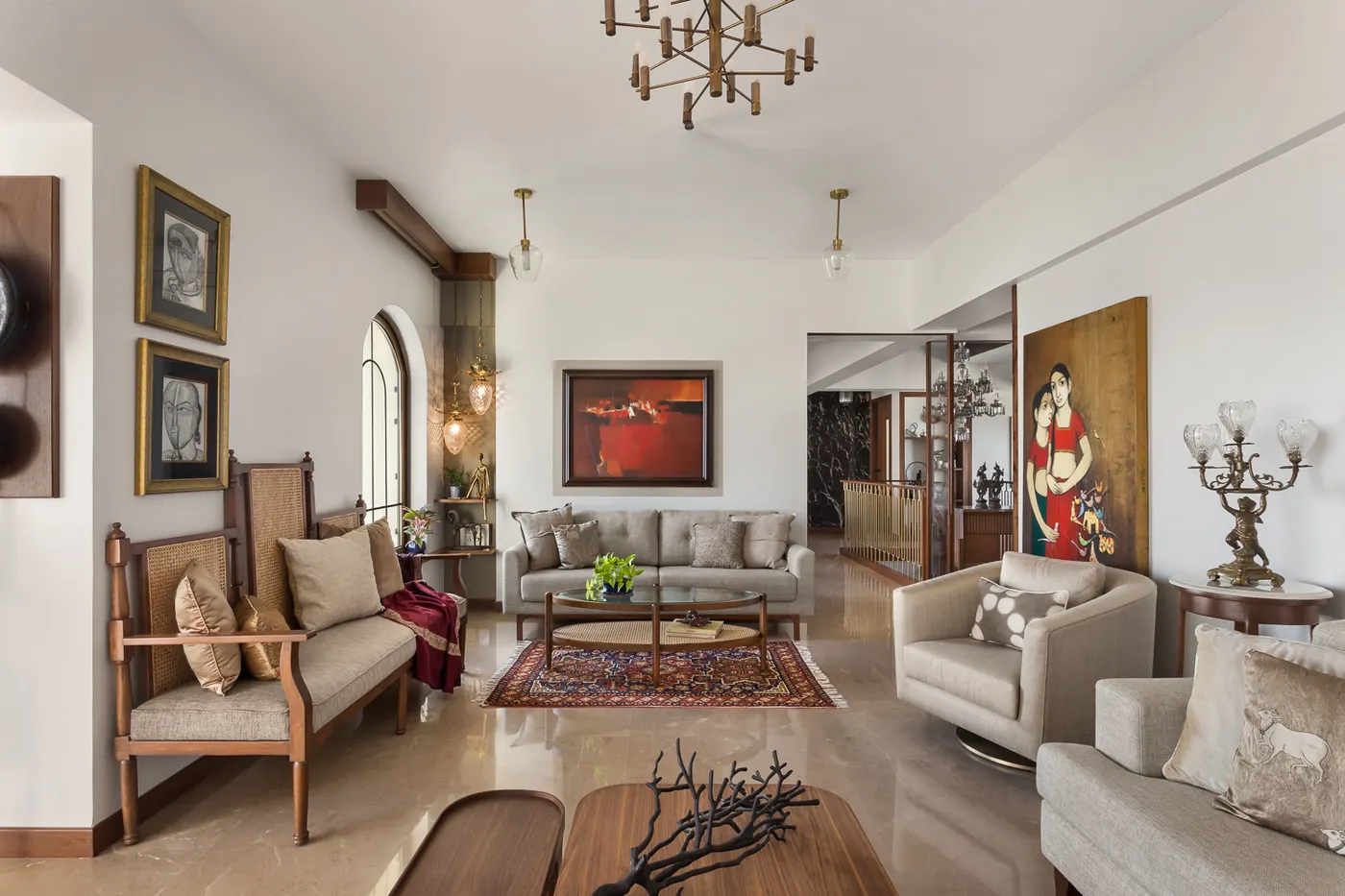 Living room at Zara with a cane-backed settee, framed drawings, a large red abstract painting and a figurative painting on a pale marble floor.