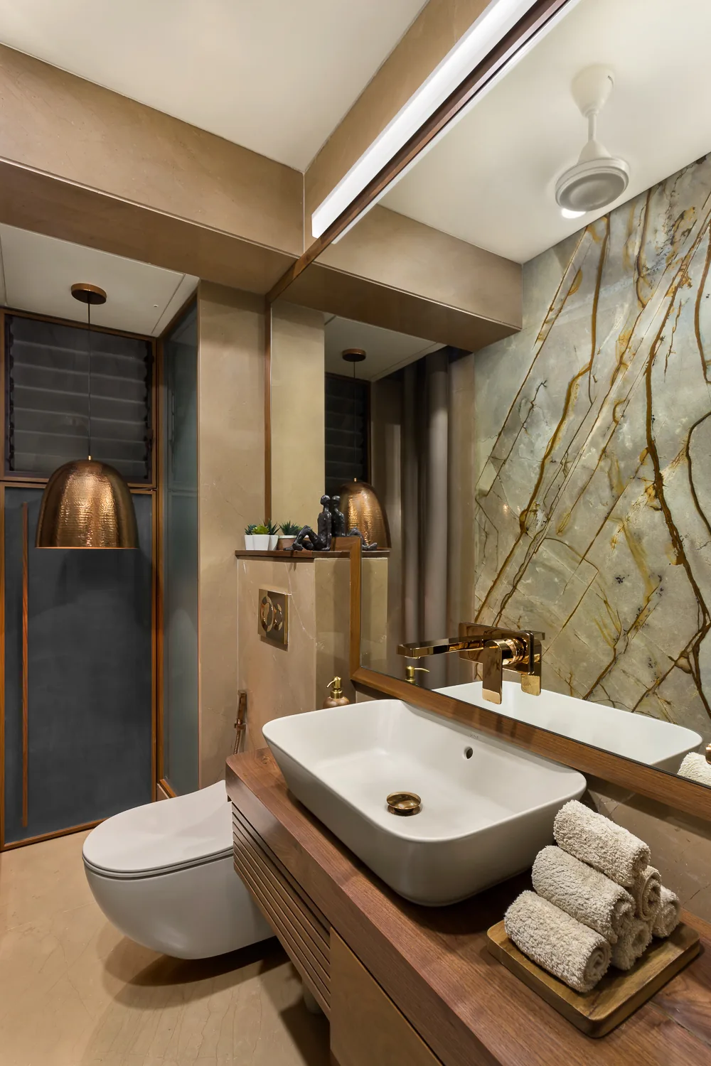 Powder room at Zara with a boldly veined stone wall, a walnut vanity and a hammered copper pendant.